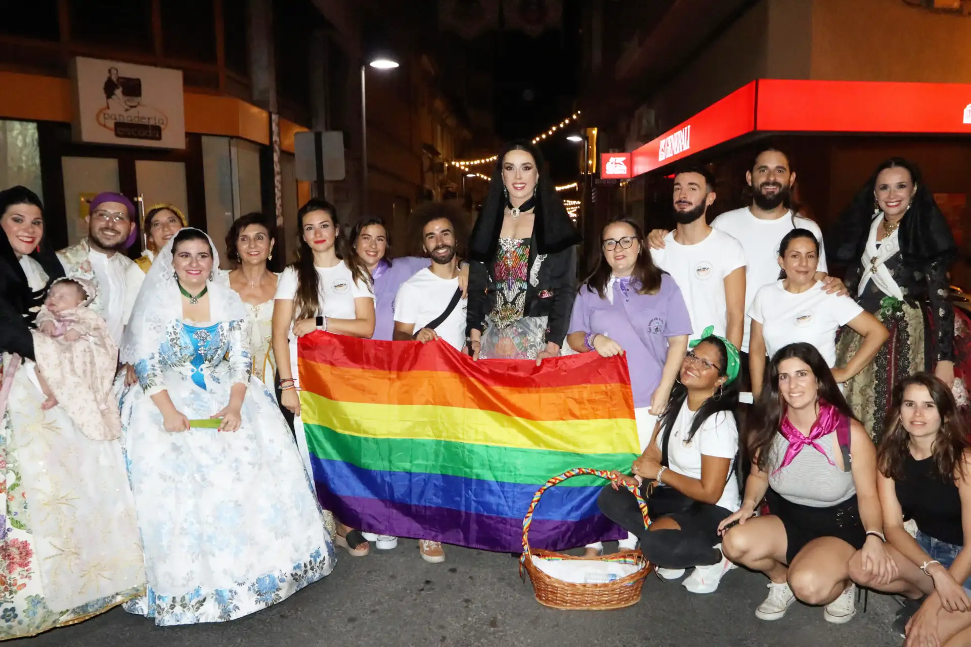 Foto de la ofrenda de las Fiestas del Cristo de San Joan en la que aparece Peter vestido con el traje tradicional rodeado de miembres de la asociación con una bandera LGTBI.