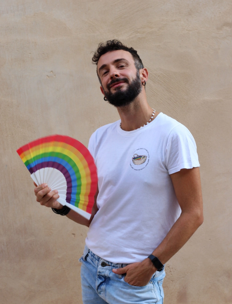 Fotografía de Joan Chápuli. Hombre delgado de unos 30 años con pelo negro y barba. Lleva un abanico arcoiris.