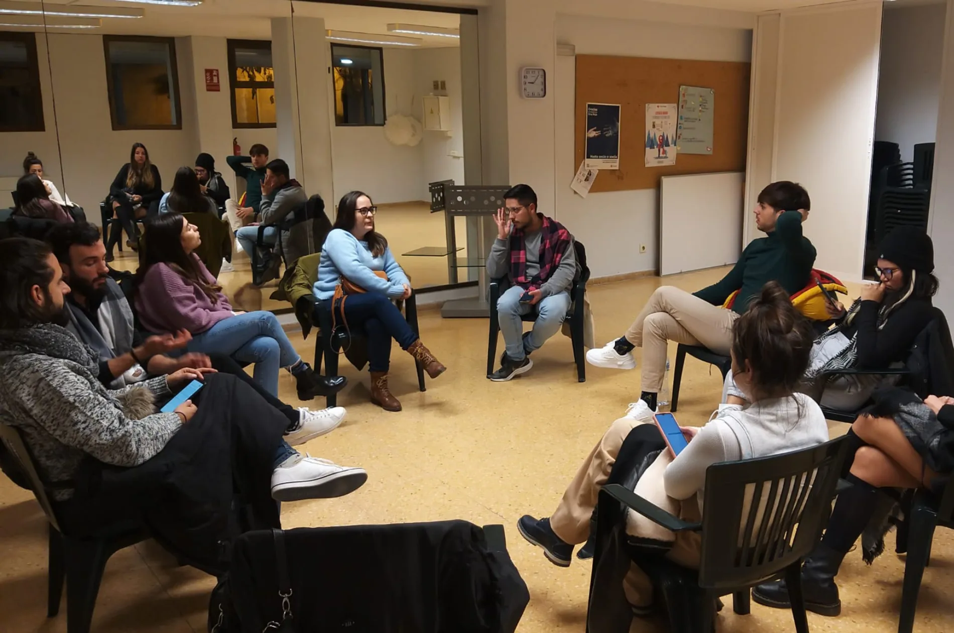 Una reunión de Colors de l'Horta en una de las salas del Cassal d'Associacions. Unos 15 miembros están en círculo sentados en sillas de plástico mientras hablan.